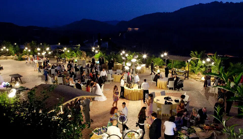 An evening reception under festoon lights at L'Agorà di Segesta, the hills darkening behind